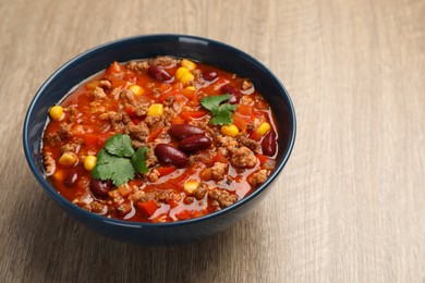 Photo of Bowl with tasty chili con carne on wooden table, closeup