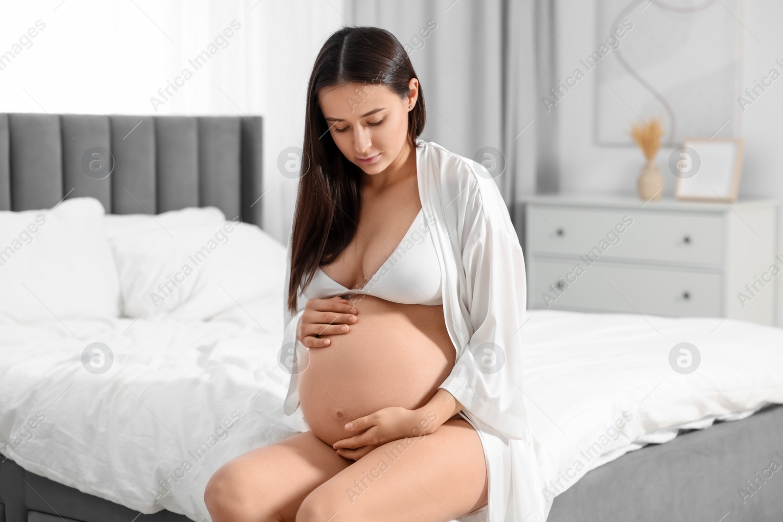 Photo of Beautiful pregnant woman in stylish comfortable underwear and robe on bed at home