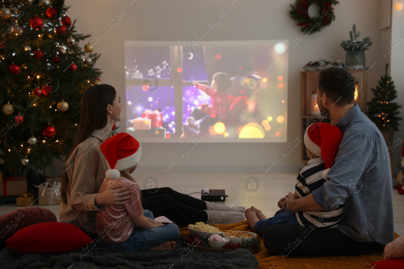 Photo of Family watching Christmas movie via video projector in cosy room. Winter holidays atmosphere