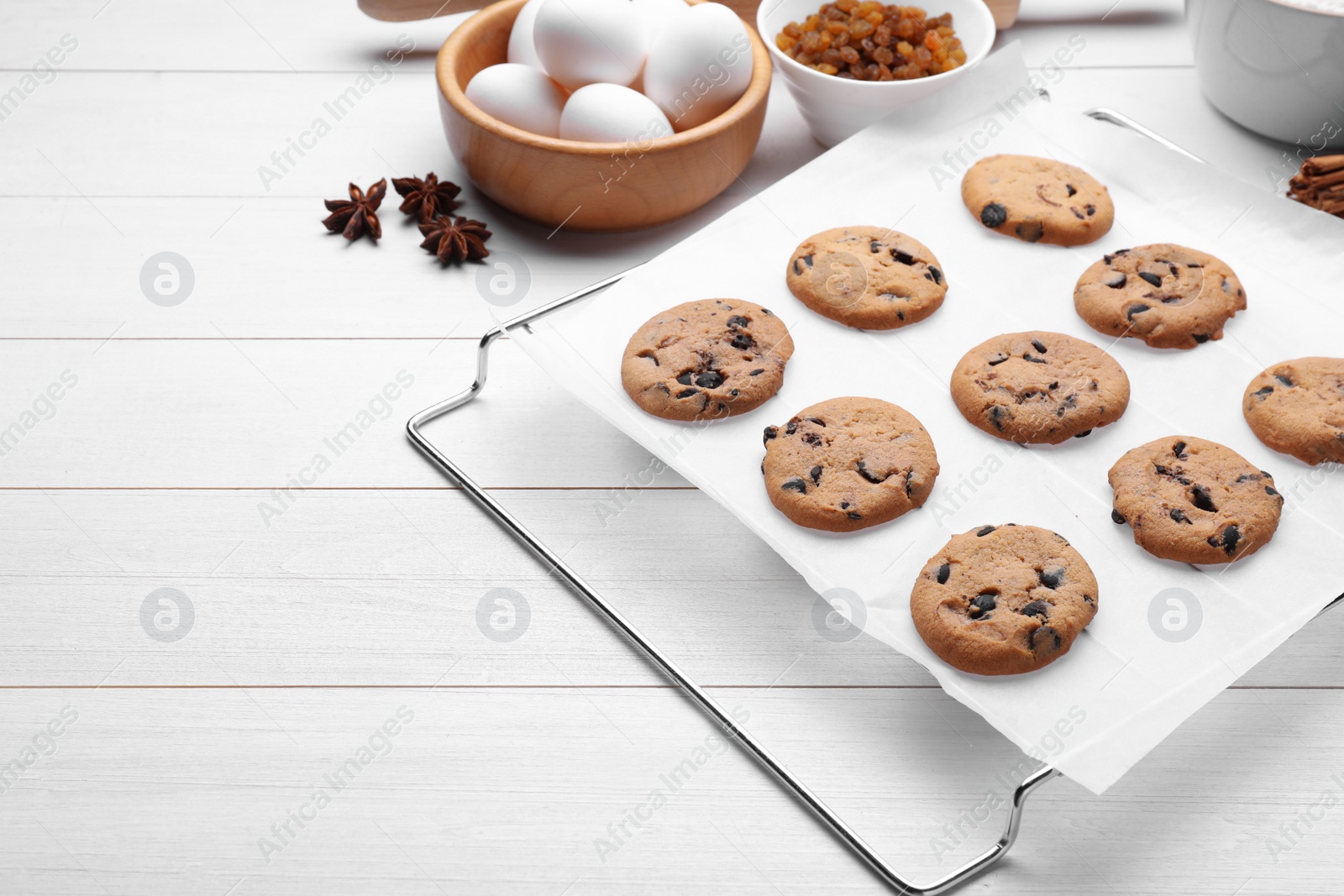 Photo of Cooling rack with parchment baking paper and tasty homemade cookies on white wooden table, space for text