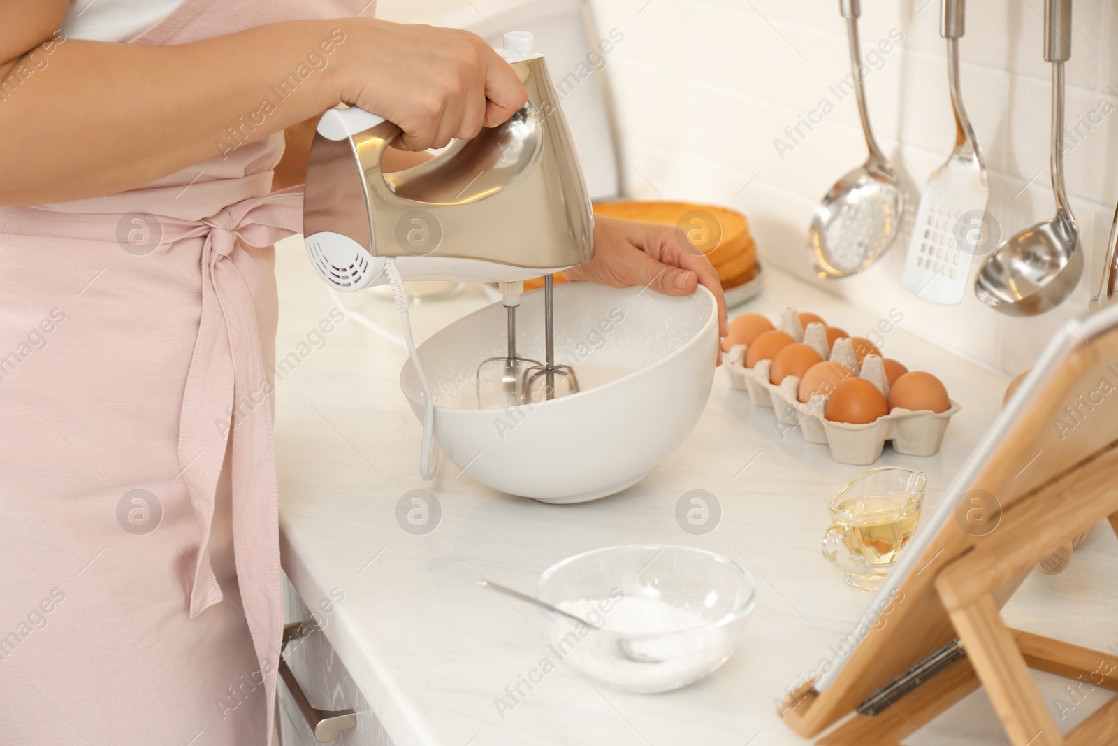 Photo of Woman making cake while watching online cooking course via tablet in kitchen, closeup