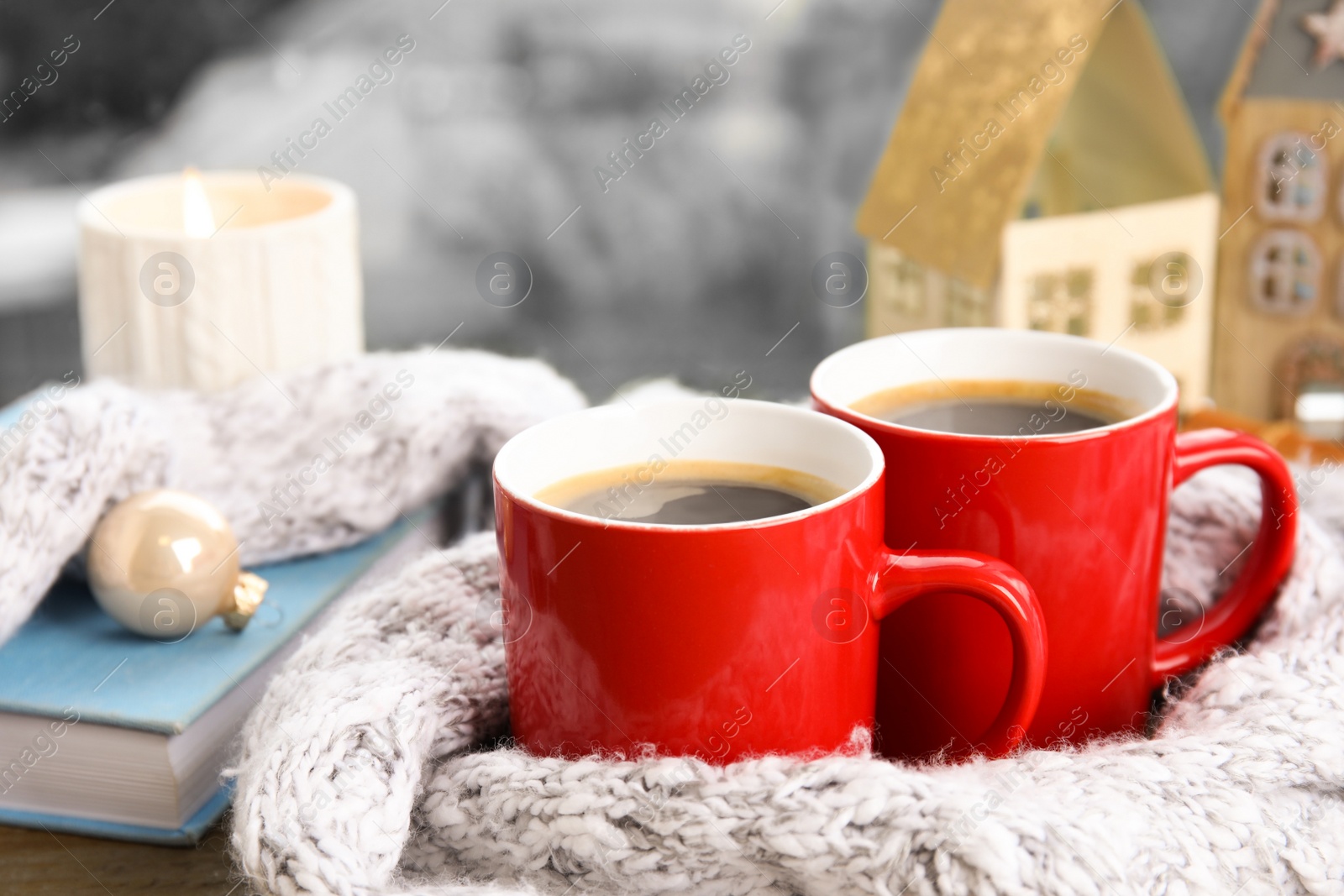 Photo of Cups of hot winter drink with scarf on window sill indoors