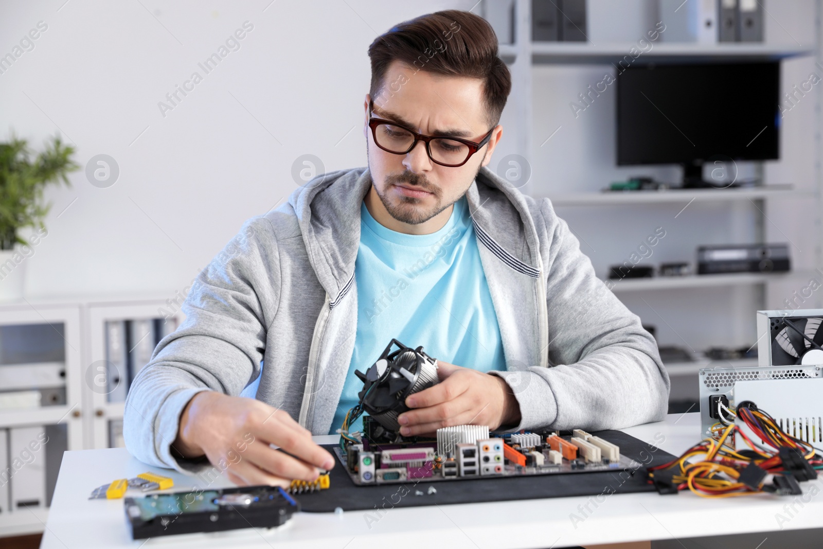 Photo of Male technician repairing motherboard at table indoors