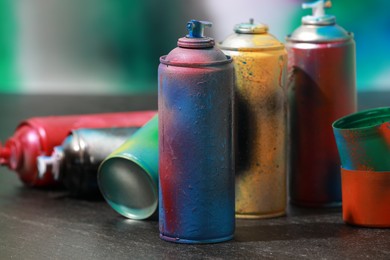 Many spray paint cans on gray surface against color background, closeup