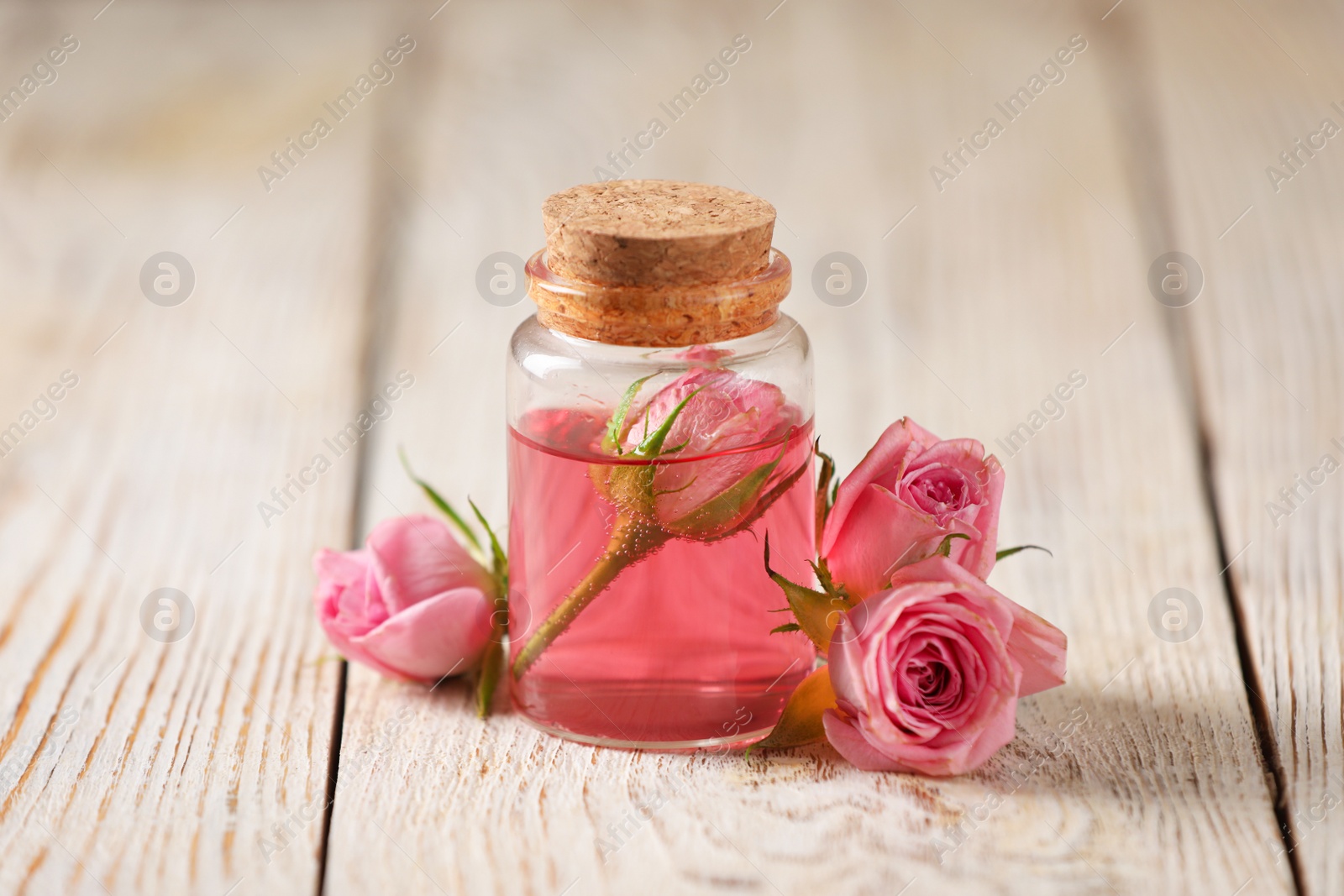 Photo of Bottle of essential rose oil and flowers on white wooden table