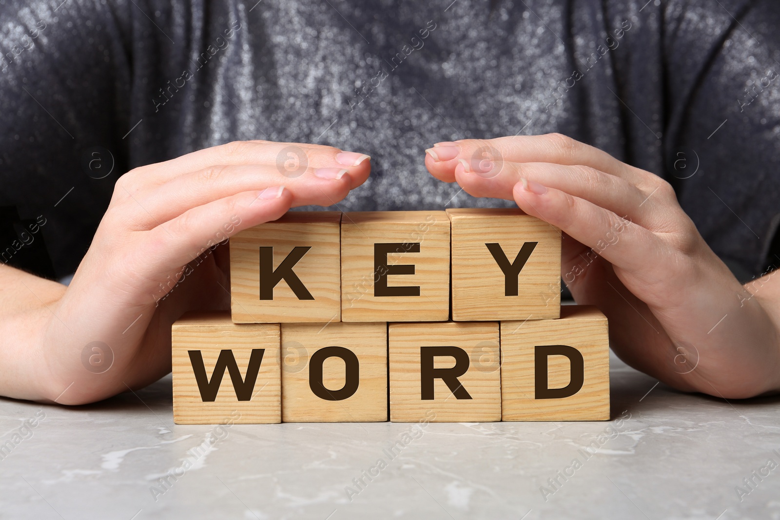 Photo of Woman demonstrating cubes with word KEYWORD at grey marble table, closeup