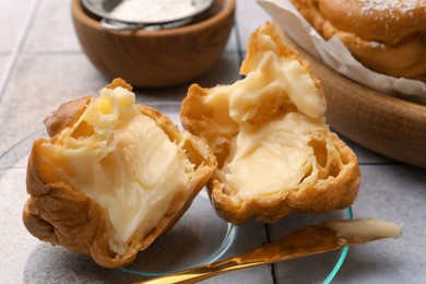 Photo of Delicious profiterole filled with cream on white tiled table, closeup