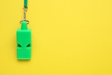 One green whistle with cord on yellow background, top view. Space for text