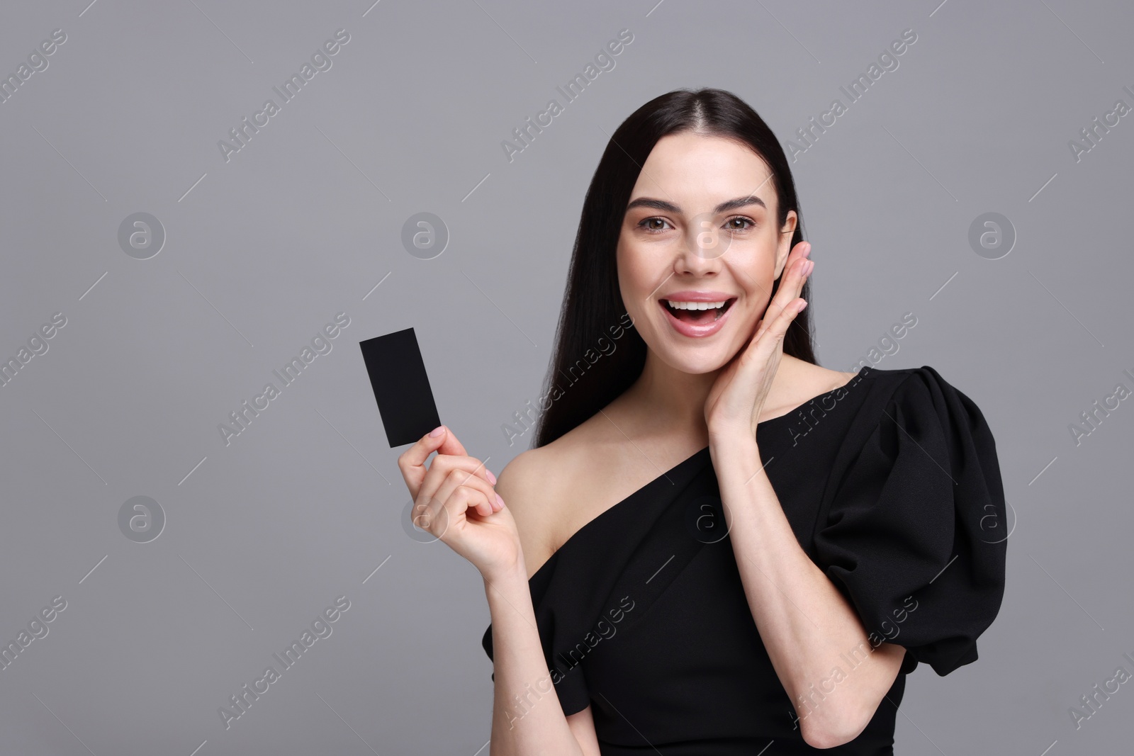 Photo of Happy woman holding blank business card on grey background. Space for text