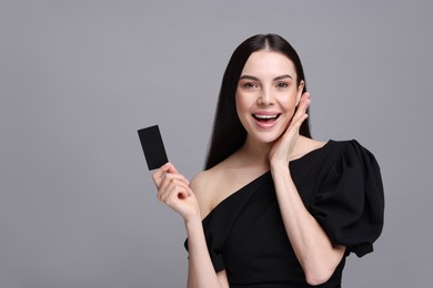 Happy woman holding blank business card on grey background. Space for text