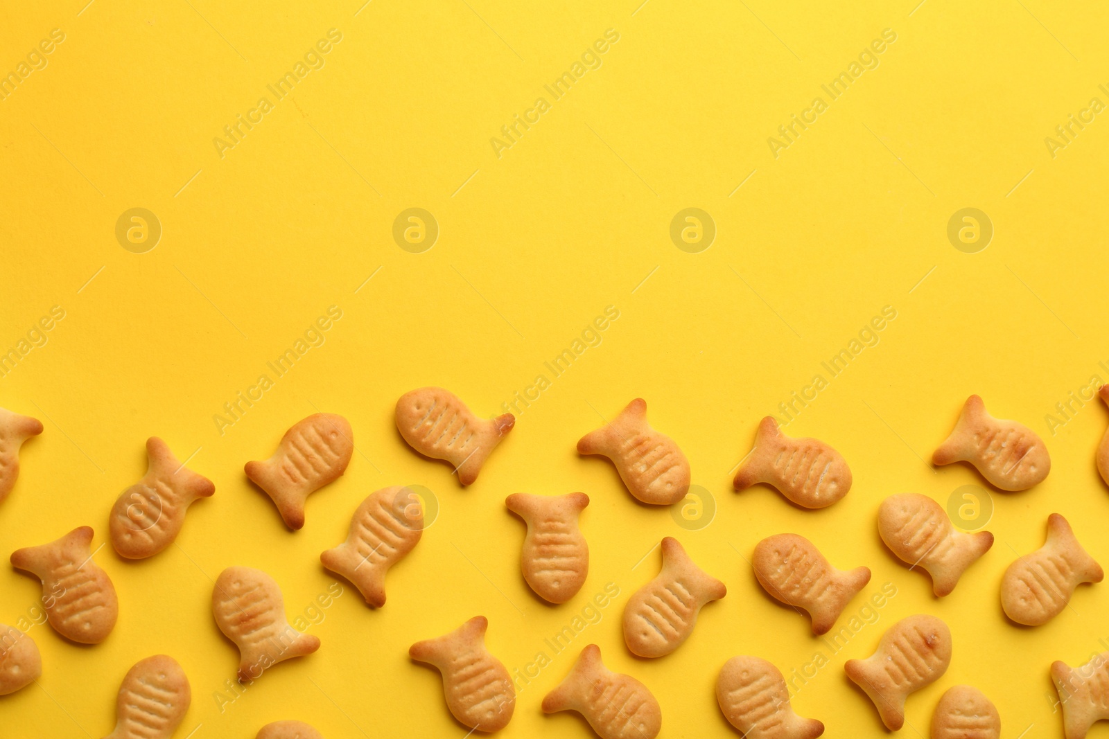 Photo of Delicious goldfish crackers on yellow background, flat lay. Space for text