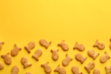 Delicious goldfish crackers on yellow background, flat lay. Space for text