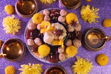 Photo of Diwali celebration. Flat lay composition with diya lamps and tasty Indian sweets on shiny violet table