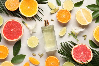 Flat lay composition with bottle of perfume and fresh citrus fruits on light marble background