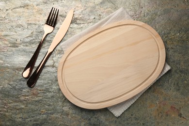 Photo of Wooden cutting board, napkin and cutlery on textured table, flat lay. Space for text