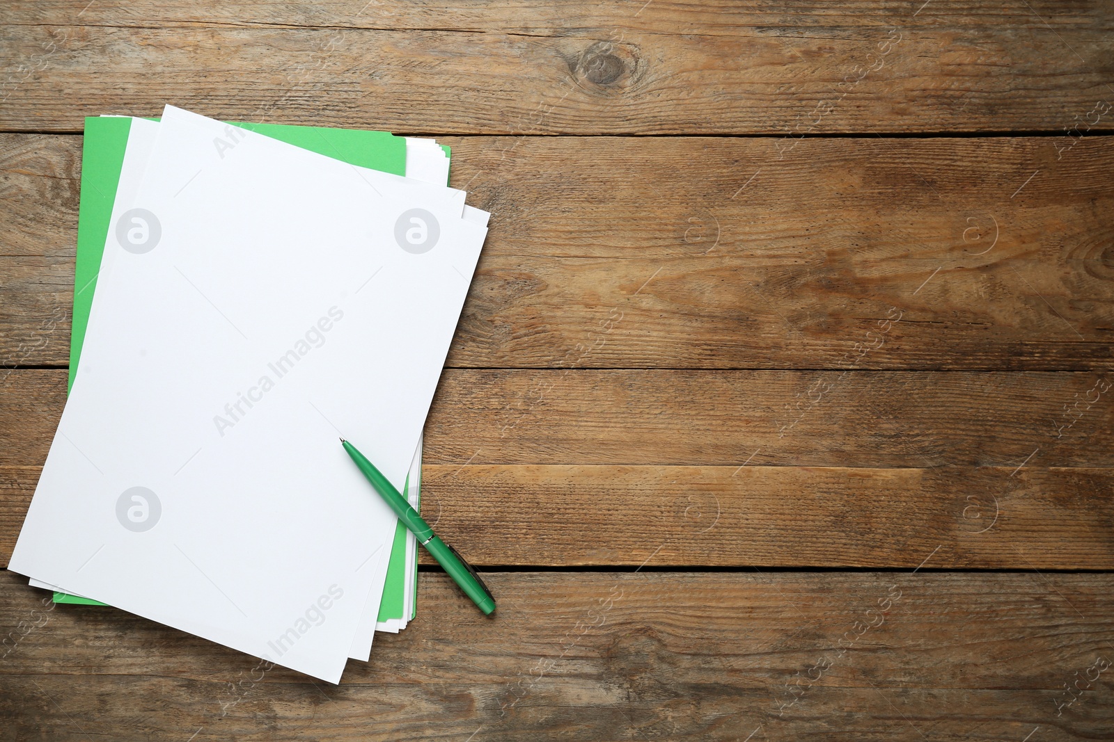 Photo of Light green file, blank sheets of paper and pen on wooden table, top view. Space for text