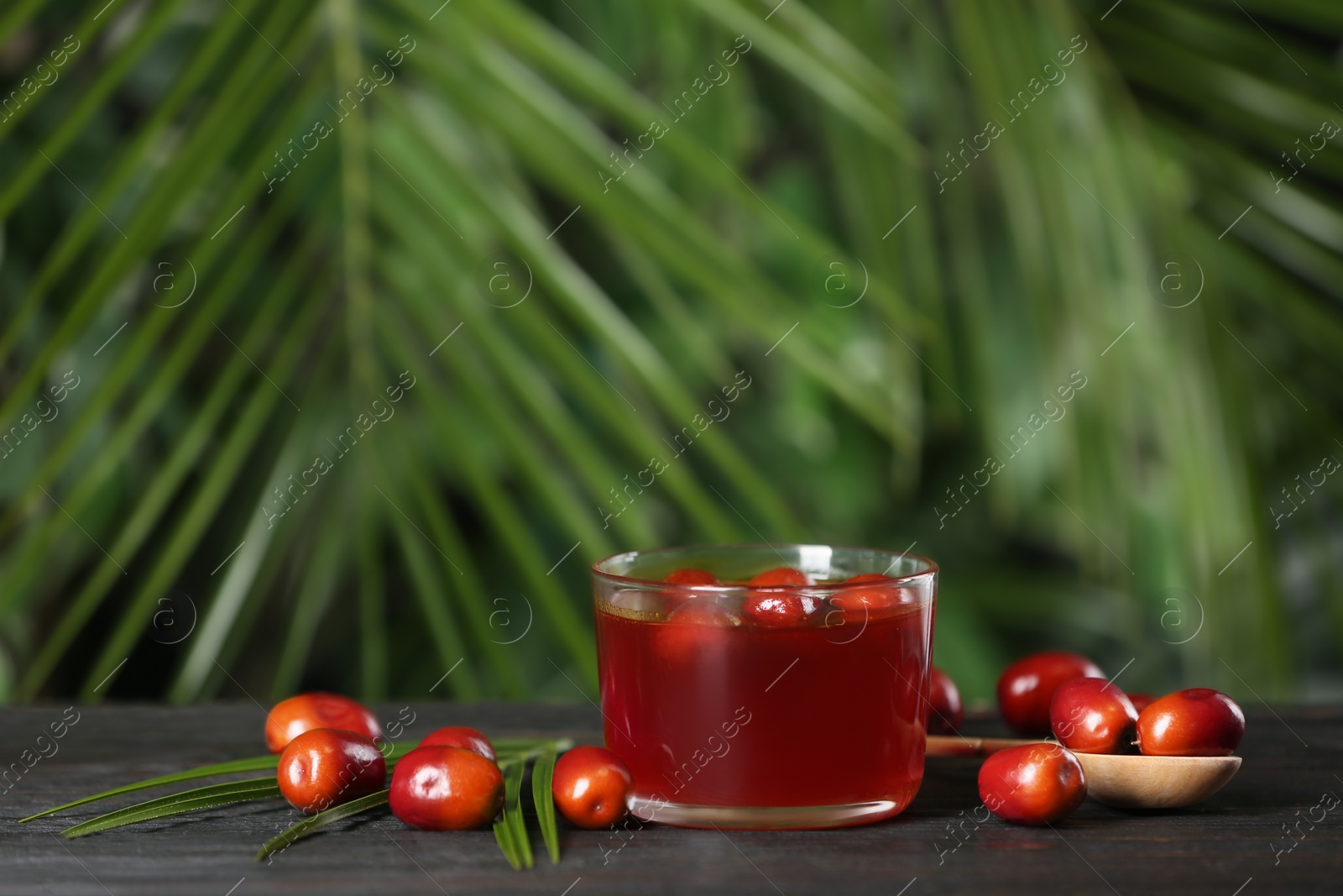 Photo of Palm oil in glass bowl, tropical leaf and fruits on wooden table. Space for text