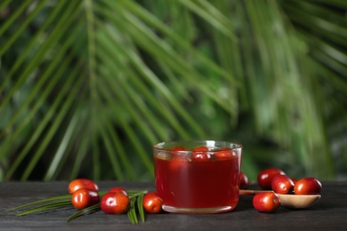 Photo of Palm oil in glass bowl, tropical leaf and fruits on wooden table. Space for text