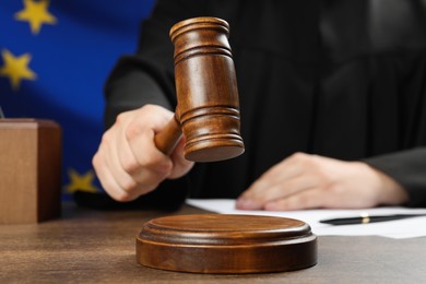 Judge with gavel at wooden table against flag of European Union, closeup