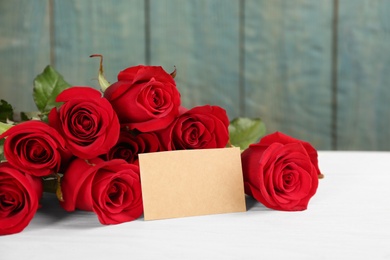 Photo of Beautiful red roses with blank card on white table, space for text. St. Valentine's day celebration