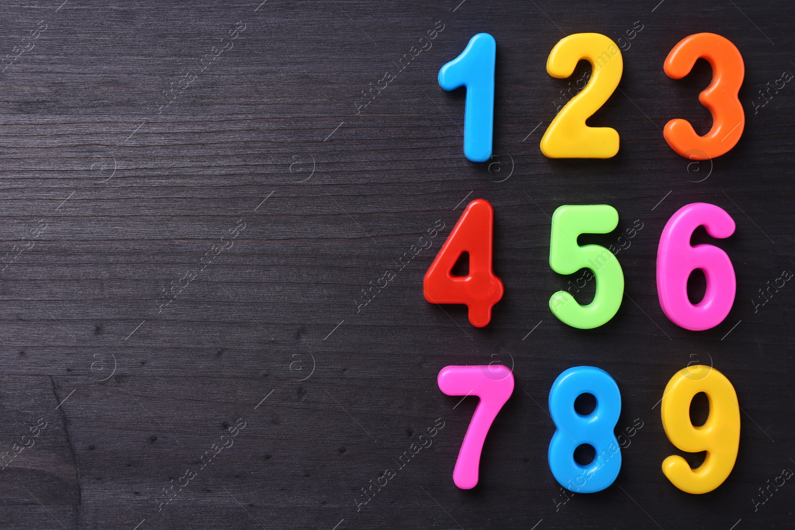 Photo of Colorful numbers on dark wooden school desk, flat lay. Space for text