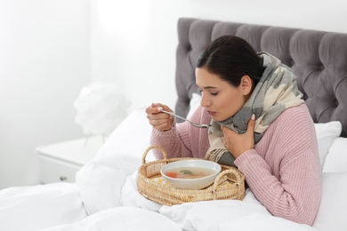 Photo of Sick young woman eating soup to cure flu in bed at home. Space for text