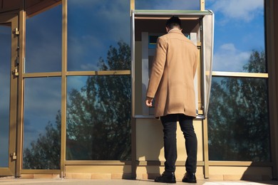 Man using modern cash machine outdoors, back view