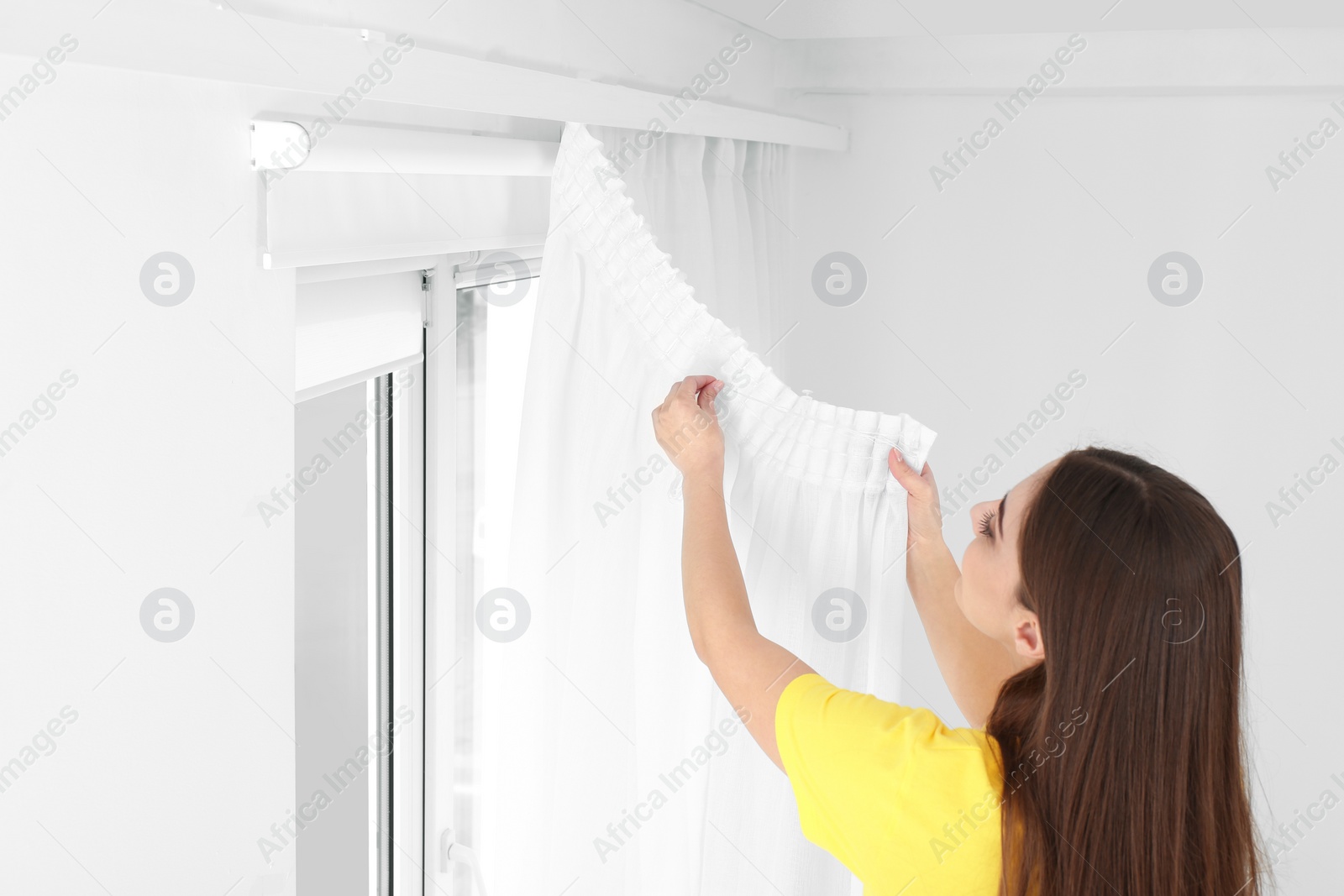 Photo of Young pretty woman hanging window curtain in room