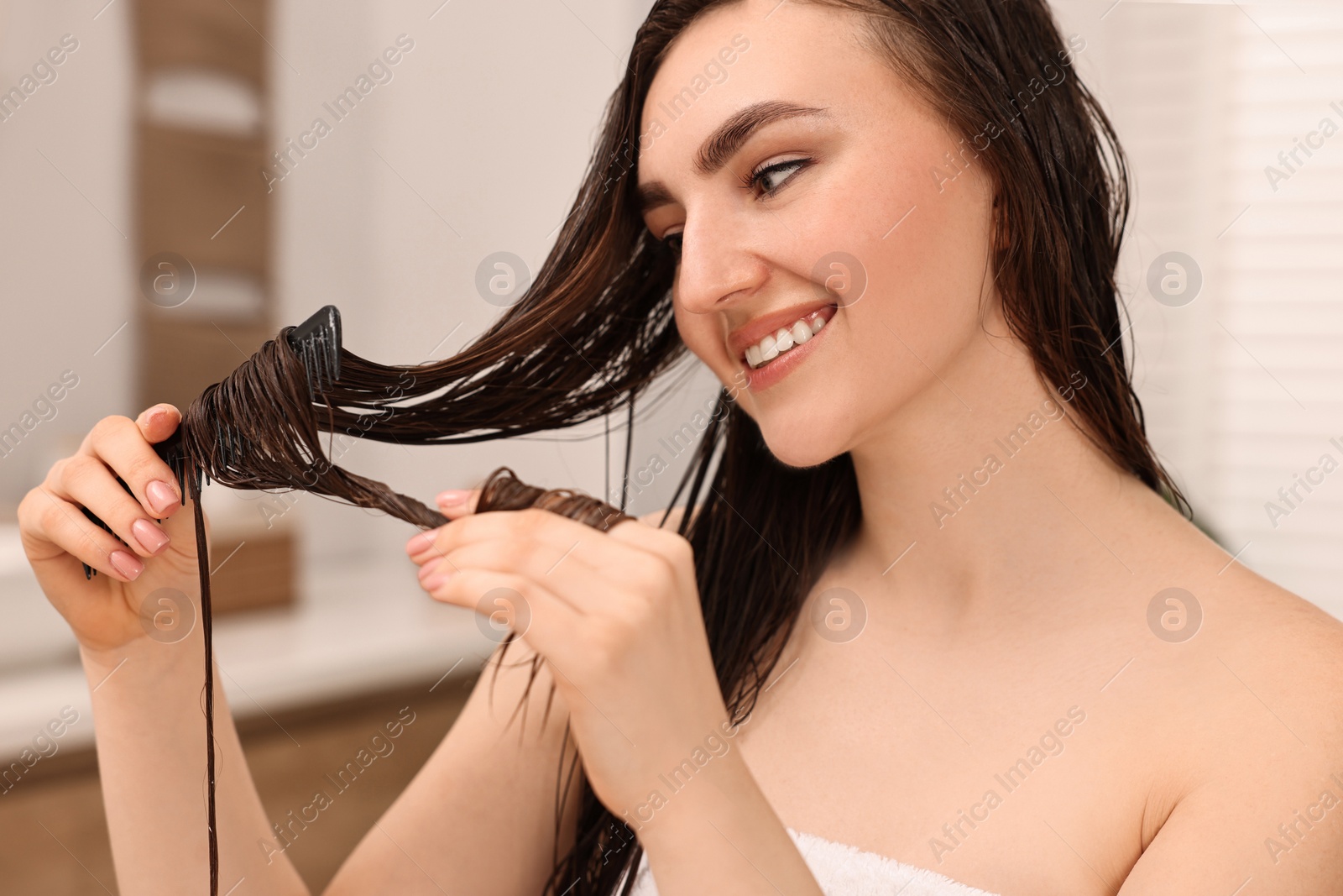 Photo of Young woman brushing hair after applying mask in bathroom