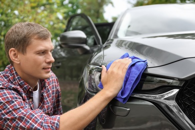 Photo of Man washing car headlight with rag outdoors