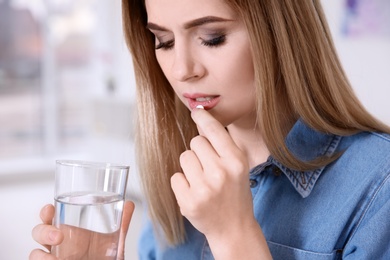 Young woman taking pill indoors