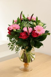 Bouquet of beautiful flowers in vase on wooden table near white wall