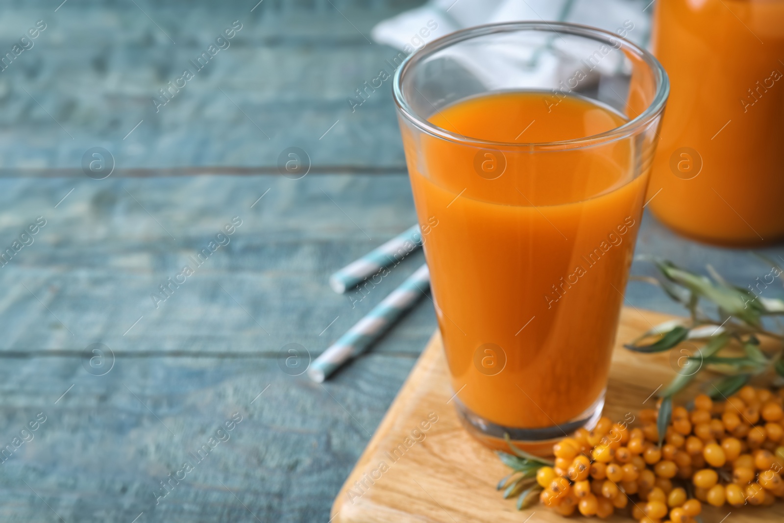 Photo of Delicious sea buckthorn juice on light blue wooden table, closeup. Space for text