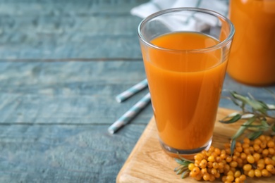 Delicious sea buckthorn juice on light blue wooden table, closeup. Space for text