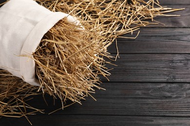 Dried straw in burlap sack on dark wooden table, space for text