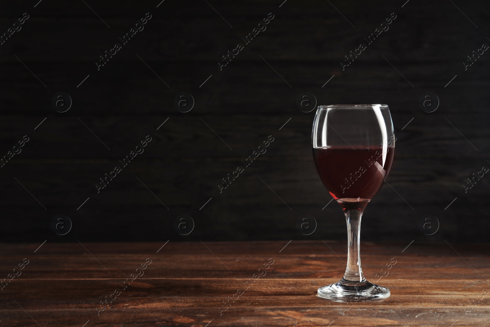 Photo of Glass with delicious red wine on table against dark background