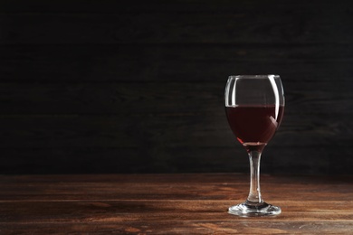 Glass with delicious red wine on table against dark background