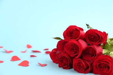Photo of Beautiful red roses and paper hearts on light blue background, space for text. St. Valentine's day celebration