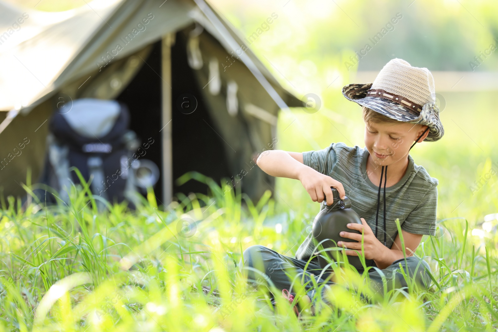 Photo of Little boy with flask near tent outdoors. Summer camp