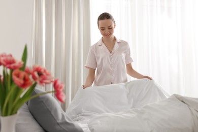 Photo of Young beautiful woman making bed in room