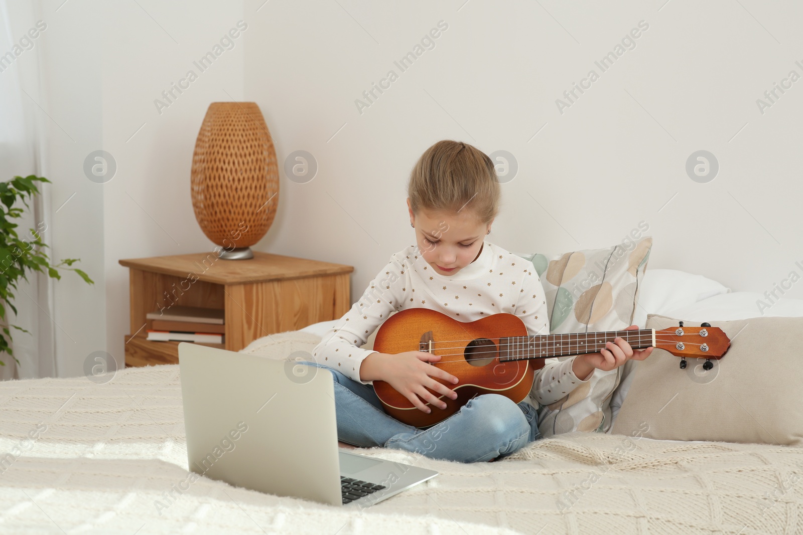 Photo of Little girl learning to play ukulele with online music course at home. Time for hobby