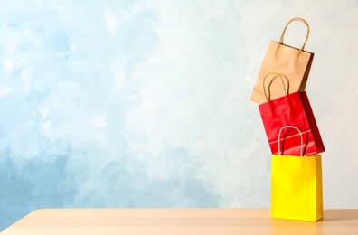 Colorful paper shopping bags on table against color background. Space for text