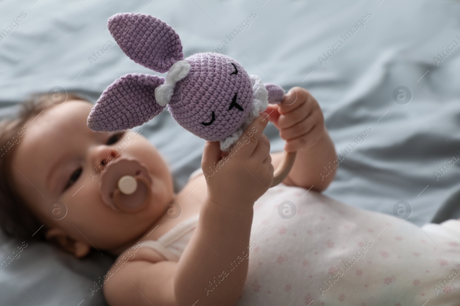 Photo of Cute little baby with pacifier and toy on bed