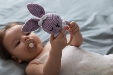 Cute little baby with pacifier and toy on bed