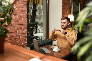 Male blogger taking photo of dessert and coffee at table in cafe