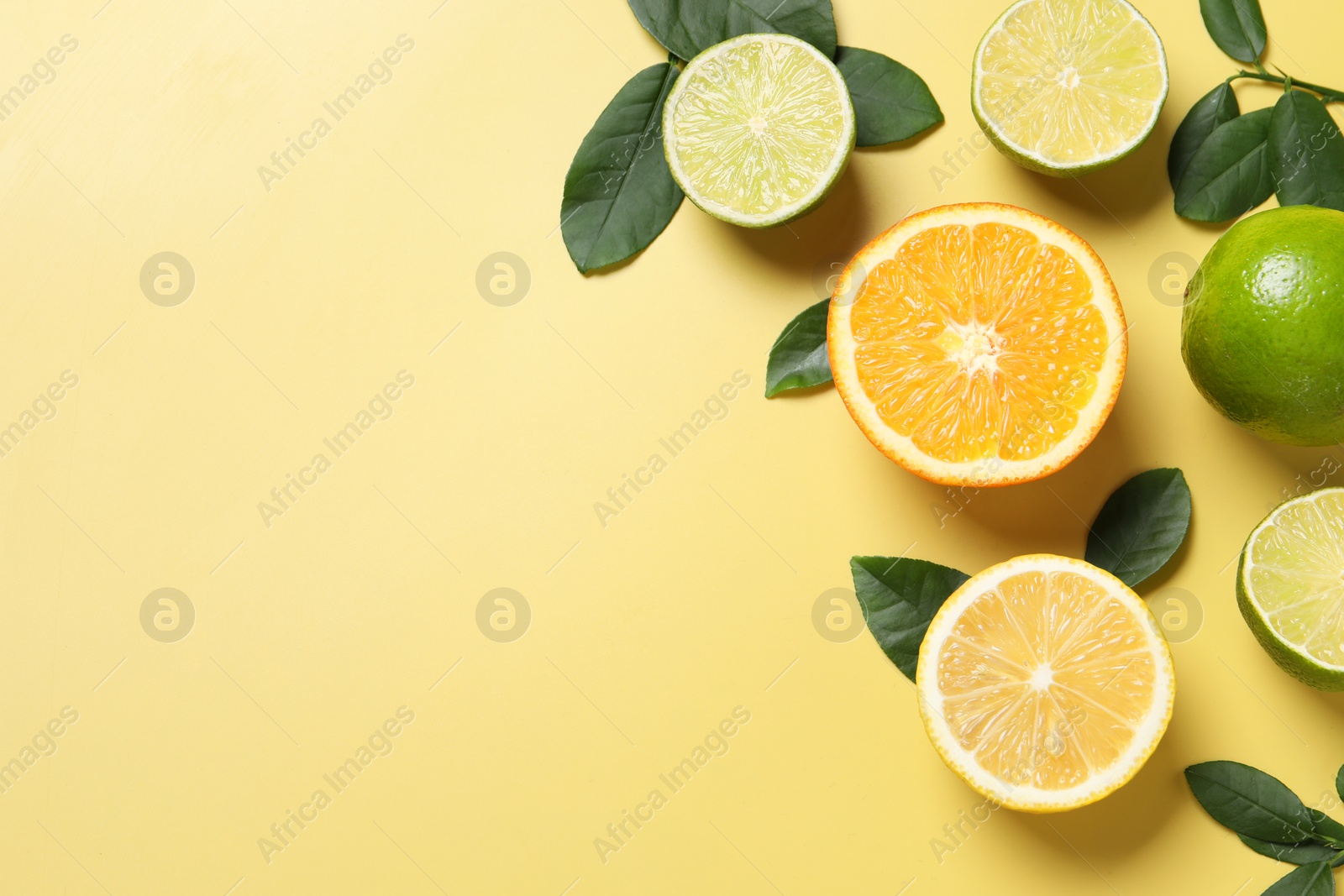 Photo of Different cut and whole citrus fruits on yellow table, flat lay. Space for text