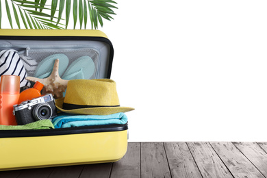Photo of Open suitcase with different beach objects on wooden table against white background. Space for text