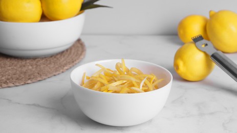 Photo of Bowl with peel pieces, fresh lemons and zester on white marble table