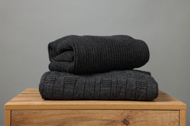 Stack of knitted sweaters on wooden table against grey background