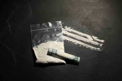 Photo of Drug addiction. Plastic bag with cocaine and rolled dollar banknote on grey textured background, flat lay